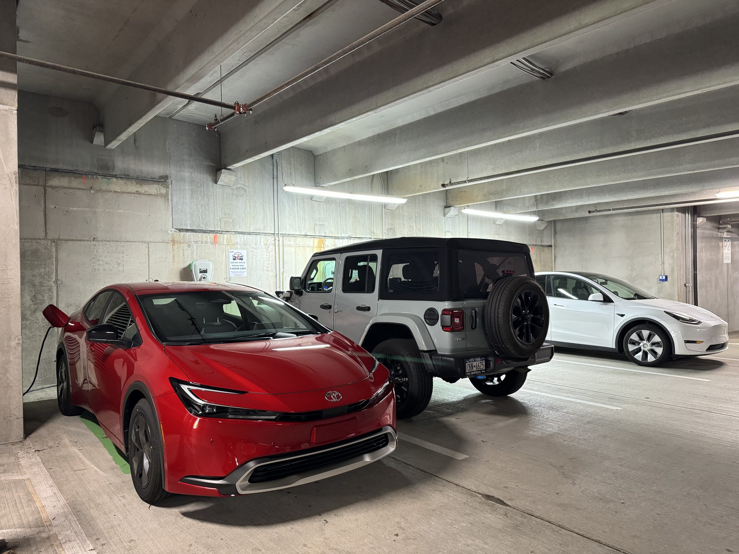 Toyota Prius Prime, Jeep Wrangler 4xe, and Tesla Model 3 on a public charger.